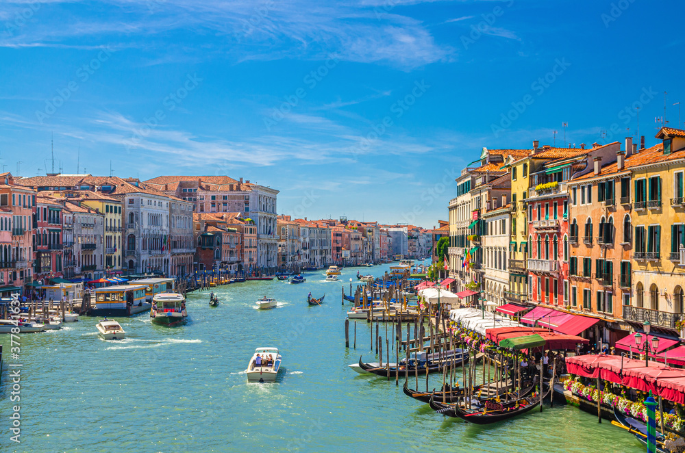 Venice cityscape with Grand Canal waterway. View from Rialto Bridge. Gondolas, boats, vaporettos docked and sailing Canal Grande. Venetian architecture colorful buildings. Veneto Region, Italy.