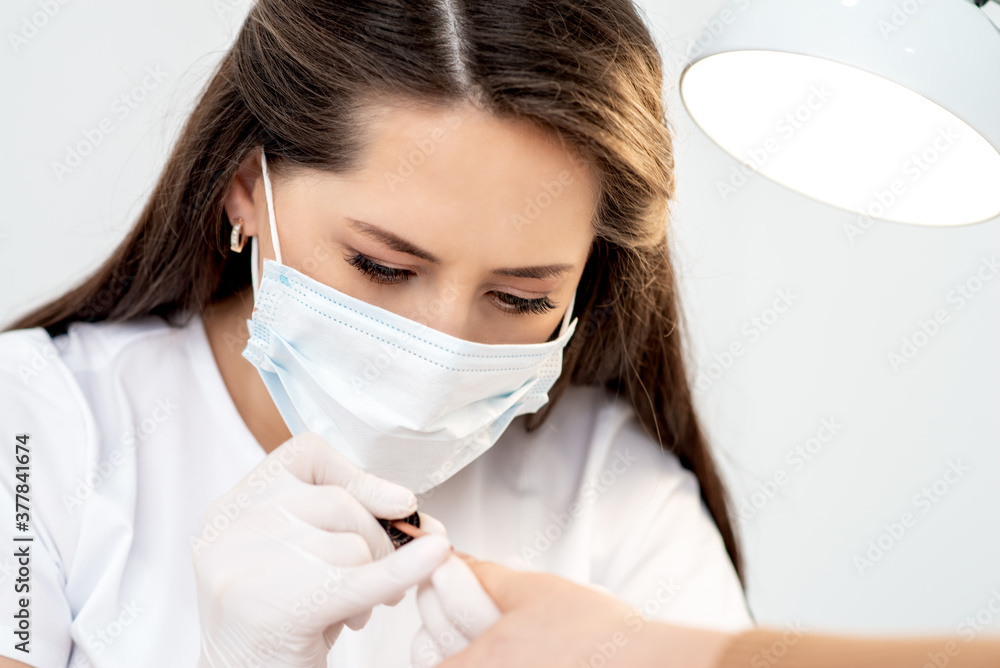 Manicure master with protective mask in rubber gloves applying beige nail polish on female nails in beauty salon Manicure master with protective mask in rubber gloves applying beige nail polish on female nails in beauty salon