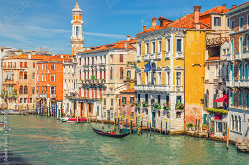 Grand Canal waterway in Venice historical city centre with sailing gondola, Palazzo Civran palace, colorful buildings and Church Holy Apostles of Christ bell tower. Veneto Region, Northern Italy.
