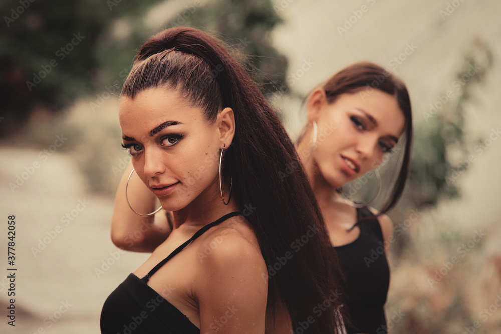 Two beautiful twin sisters Outdoor portrait. beautiful athletic slim bodied twin girls brunettes with long hair