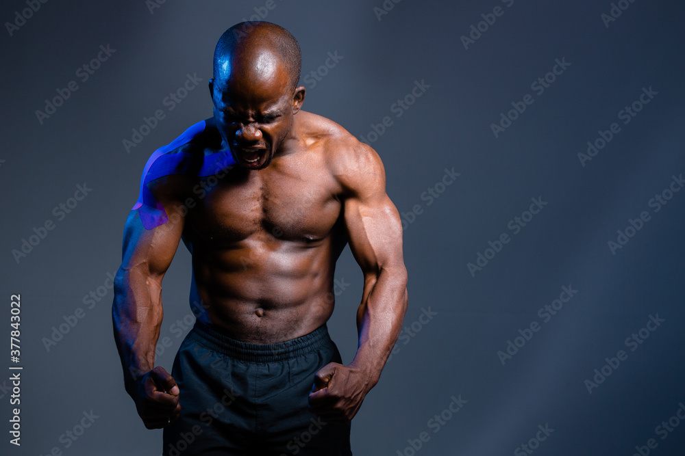 muscular african american strains muscles and screams. Man isolated on gray background