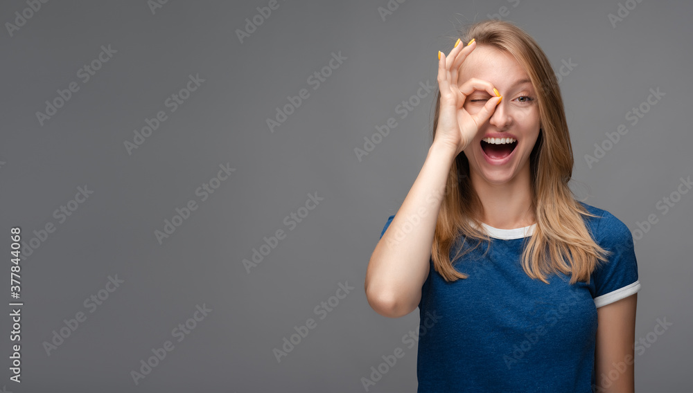 Cheerful female looking at the camera through fingers in OKAY gesture. Face expressions, emotions concept. Copy space Cheerful female looking at the camera through fingers in OKAY gesture. Face expressions, emotions concept. Copy space