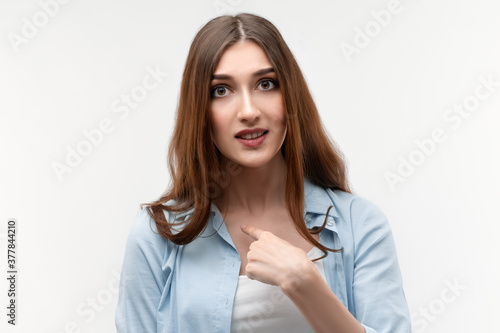 Indignant brunette female points at herself with for finger, has dissatisfied expression. Facial expression concept