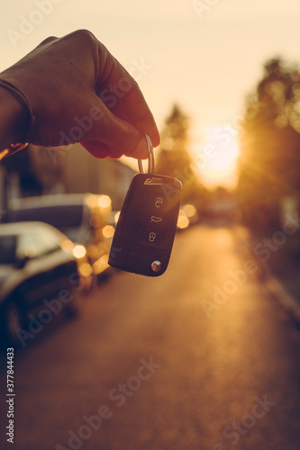 Eine Hand hält einen Autoschlüssel vor einer Straße im Gegenlicht. 