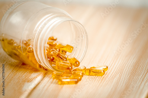Capsules of fish oil spilled out open container. Shot in studio isolated on wooden table
