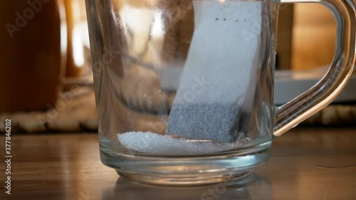 Taking electric ketle and pouring water inside a glass cup with sugar and tea bag for tea preparation. Home cooking photo