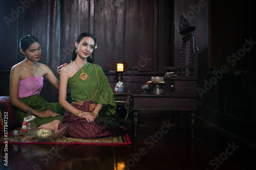 Beautiful Asian woman wearing in Thai dress costume traditional according Thai culture and tradition let the maid take care the beauty at the ancient house Ayutthaya, Thailand