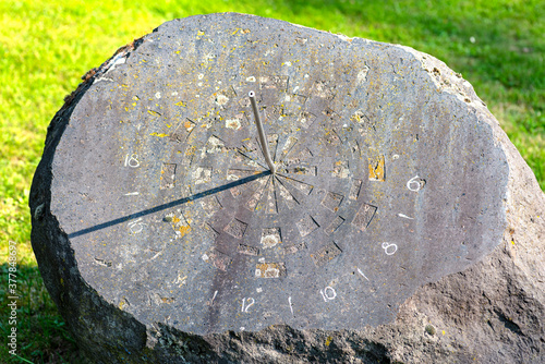 An old sundial made of a large stone with a metal rod, the clock will start at 4 PM. photo