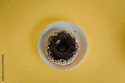 Black round donut at bright yellow background with coffee glass
