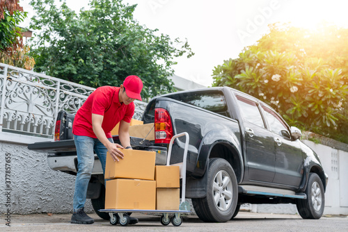 Delivery men in red uniform unloading cardboard boxes from pickup truck. Courier man sending the parcel or package to the customer on a business day. Online shopping and transport logistics concept.