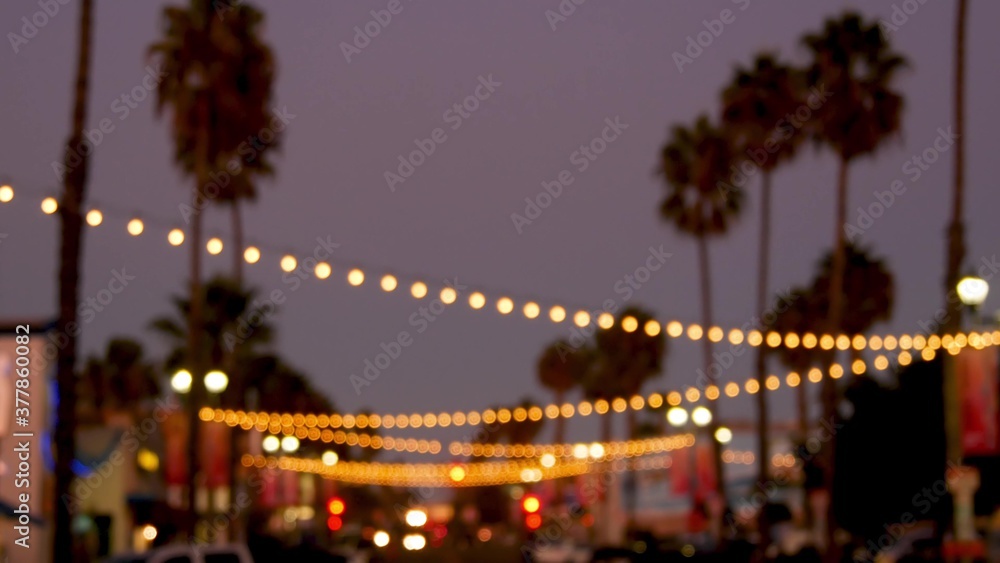 Decorative staring garland lights, palm trees silhouettes, evening sky. Blurred Background. Street decorated with lamps in California. Festive illuminations, beach party, tropical vacations concept. Decorative staring garland lights, palm trees silhouettes, evening sky. Blurred Background. Street decorated with lamps in California. Festive illuminations, beach party, tropical vacations concept.