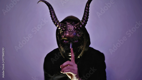 a person wearing a horned mask isolated on a purple lit background. photo