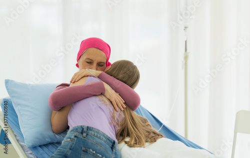 Young adult female cancer patient spending time with hug her daughter on bed at hospital. family support concept. photo