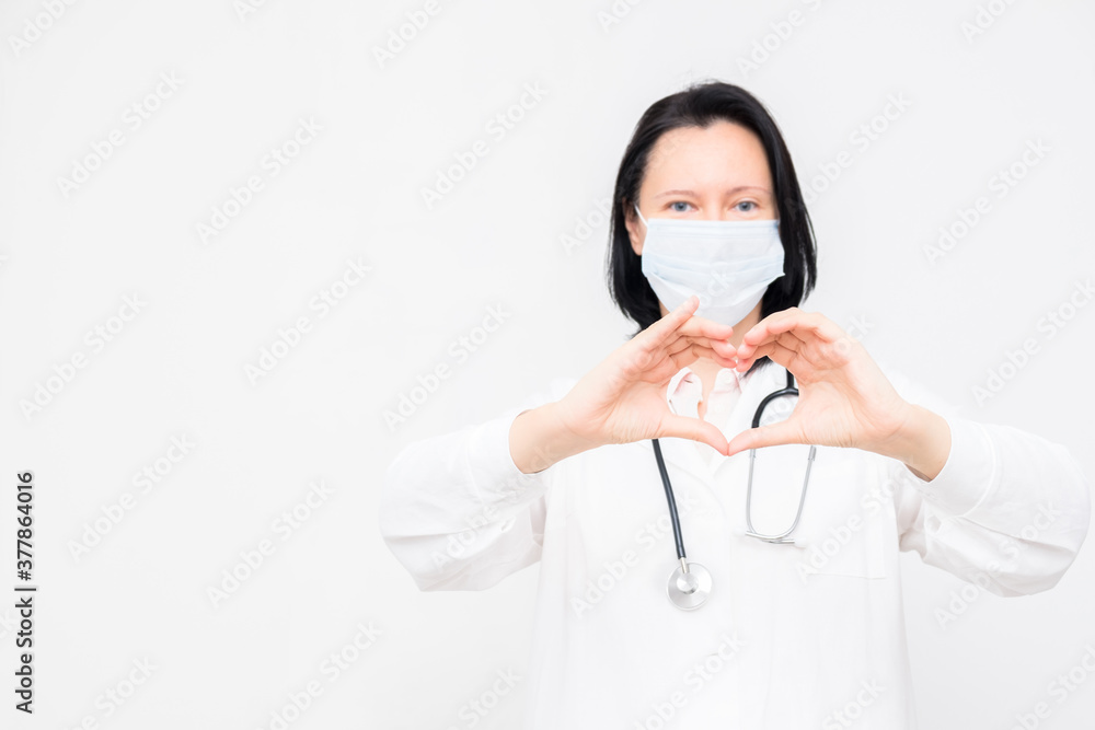 Woman doctor in medical mask shows heart symbol on white background with copy space Woman doctor in medical mask shows heart symbol on white background with copy space
