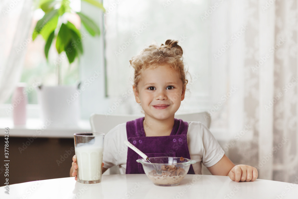 Charming girl eats cereal with milk for Breakfast and . On the table are chocolate flakes, a glass of milk. Healthy Breakfast, taking care of children. Space for text Charming girl eats cereal with milk for Breakfast and . On the table are chocolate flakes, a glass of milk. Healthy Breakfast, taking care of children. Space for text