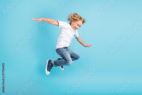 Profile photo of young boy jump fly movement hands wear white shirt jeans sneakers isolated blue color background photo