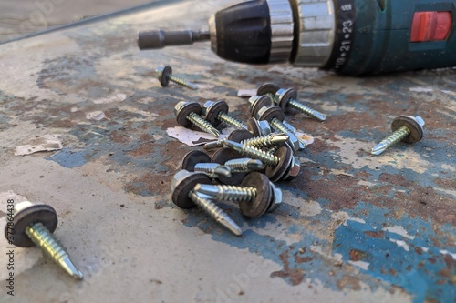 Construction tool. Tapping screws made of steel. Cordless drill on background.