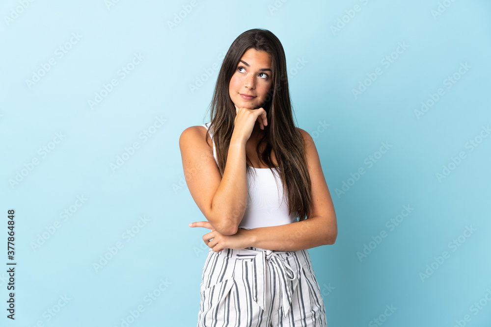 Young brazilian woman isolated on blue background and looking up Young brazilian woman isolated on blue background and looking up