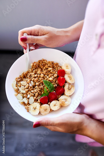 Woman eating healthy breakfast bowl  hold in hand granola  seeds  fresh strawberry  banana  top view  copy space. Clean eating  detox  dieting  vegetarian food concept