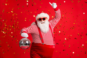 Photo of retired old man grey beard hold vintage disco ball dance funky wear santa x-mas costume suspenders sunglass gloves striped shirt cap isolated red color background