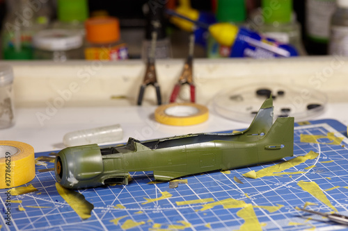 Plastic case of combat aircraft with new painting of khaki color, assembled and painted by hand. Special equipment for avia modelling hobby on background, dirty fragmented measuring pad with spots.
