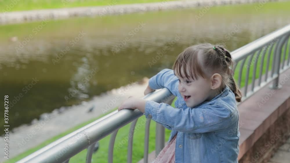 Happy little girl walks by the railing in the park.
