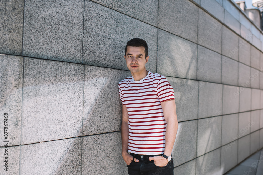 Positive young man leaning on concrete wall in city street Positive young man leaning on concrete wall in city street