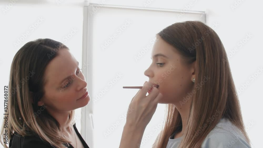 Close up makeup artist making professional make-up for young woman in beauty studio. Make up Artist applying lipstick on model