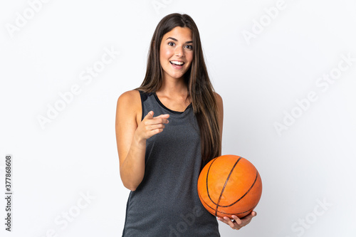 Young brazilian woman playing basketball isolated on white background surprised and pointing front © luismolinero