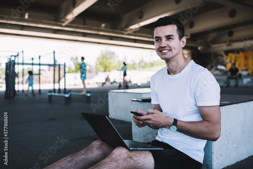 Happy guy browsing smartphone near street gym complex