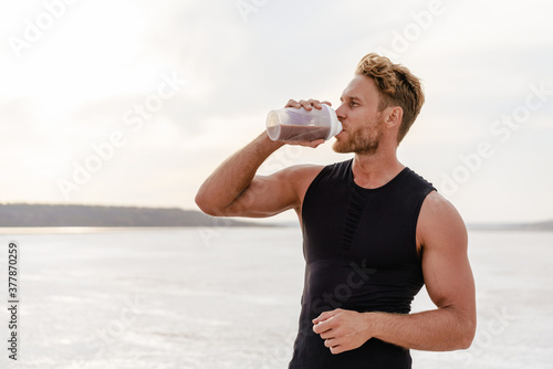 Fototapete Image of young athletic sportsman drinking protein shake