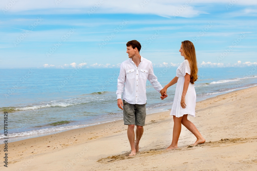 Cute couple of young lovers walk along the beach