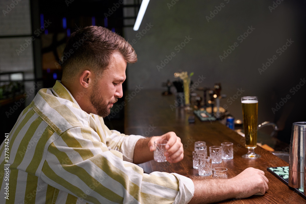 depressed young caucasian man in bar. thoughtful male has melancholic mood with a glass of strong alcohol. unlucky date