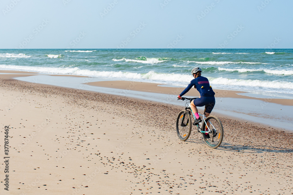 Girl riding a bike on a beautiful sandy beach with rough Baltic Sea on background