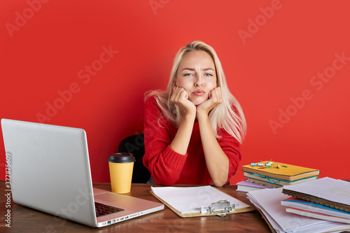 sleepy blonde puzzled caucasian woman employee in office sit work at desk, she has no energy to work, isolated red background photo