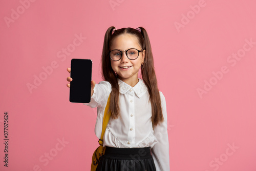 Technology and school. Little child in glasses in uniform showing phone