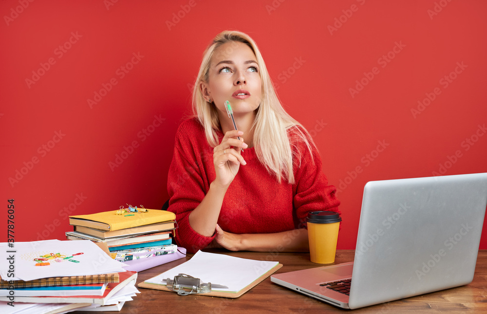 portrait of thoughtful caucasian female at work place, she is contemplation, having too much work, deadlines. sit with laptop isolated over red background portrait of thoughtful caucasian female at work place, she is contemplation, having too much work, deadlines. sit with laptop isolated over red background