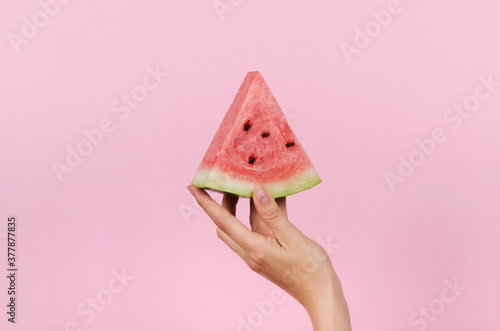 Hand holding slice of watermelon on pink background