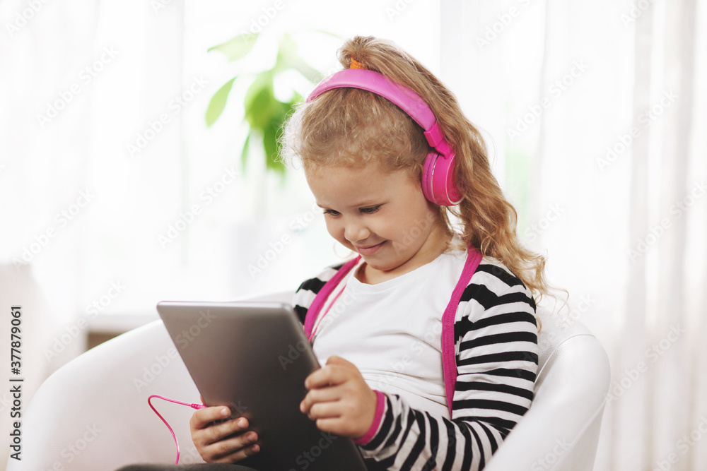 A school girl in pink headphones sits with a tablet and listens to an online lesson. Online education, online training, social distance A school girl in pink headphones sits with a tablet and listens to an online lesson. Online education, online training, social distance