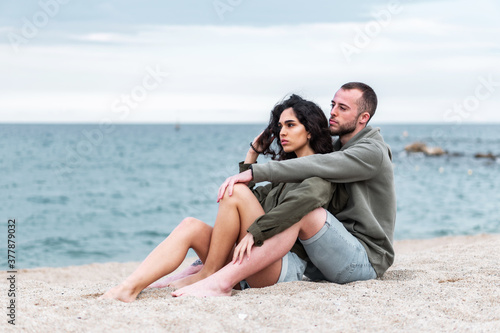 Young couple being sweet and romantic sitting at the beach. Millennial Girlfriend and Boyfriend together at an outdoors photoshoot. People enjoying the beach © David CJ Photography