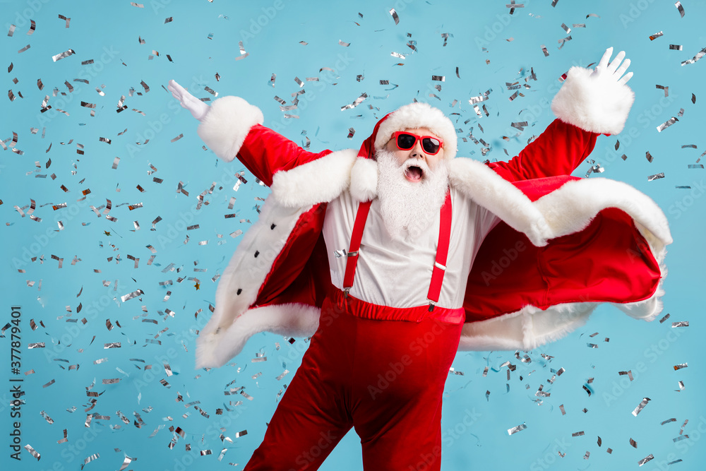 Obraz premium Photo of pensioner old man grey beard carefree raise hands dance open mouth pretend flying angel confetti wear santa x-mas costume suspender sunglass headwear isolated blue color background