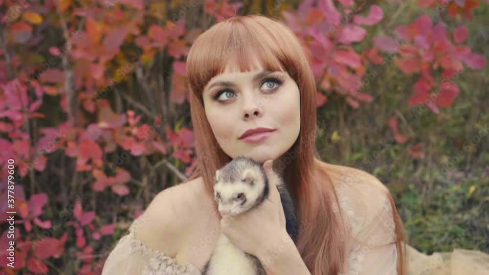 Portrait of a young beautiful woman who holds a little ferret in her arms. She looks with love and affection for her pet. Vintage medieval clothing on a background of autumn nature Portrait of a young beautiful woman who holds a little ferret in her arms. She looks with love and affection for her pet. Vintage medieval clothing on a background of autumn nature