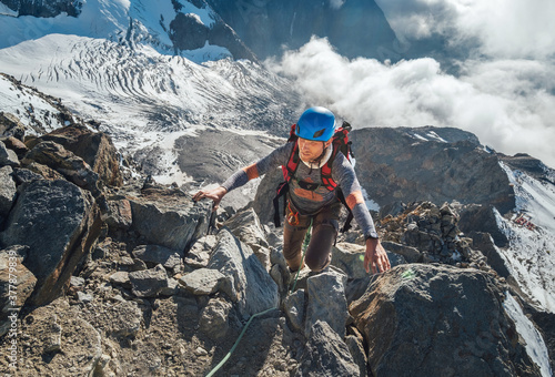 Climber in a safety helmet, harness with backpack ascending a rock wall with Bionnassay Glacier on background and looking at the summit during Mont Blanc ascending,France route.Active climbing concept