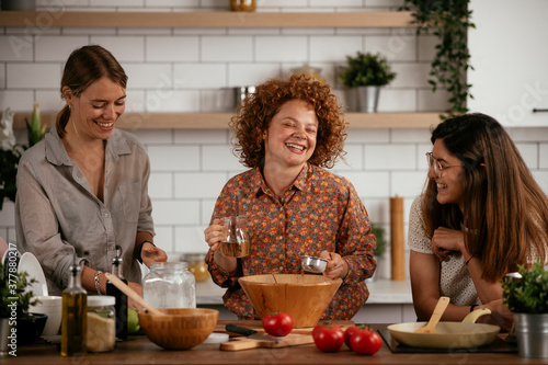 Girlfriends having fun in kitchen. Young girls preparing delicious food at home.