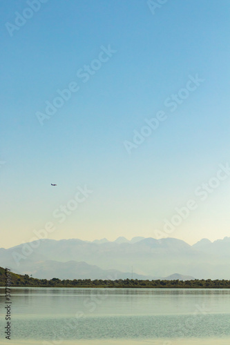Beautiful minimalistic photo of an airplane in the sky over mountains and lake, desktop wallpaper © FellowNeko