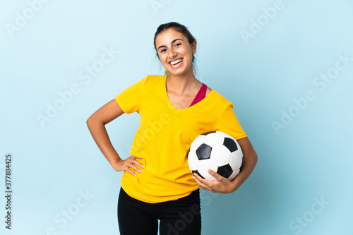 Young hispanic football player woman over isolated on blue background posing with arms at hip and smiling © luismolinero
