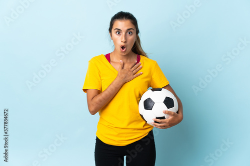 Young hispanic football player woman over isolated on blue background surprised and shocked while looking right © luismolinero