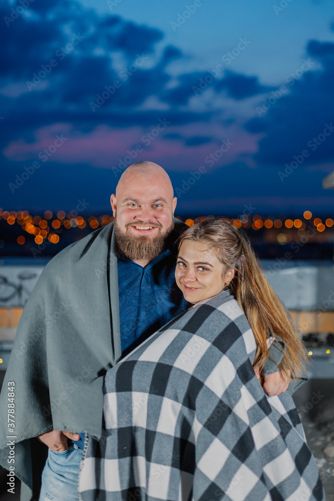 Beautiful couple on the roof under a blanket in the evening.