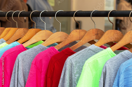 Multicolored shirts and sweatshirts hang on wooden hangers close up.