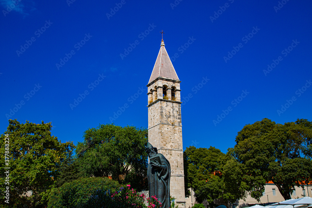 Estatua de bronce con torre campanario  de arcos y tejado en punta